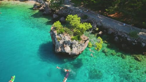 Vibrant Brela beach with rocky cliff in Croatia, with clear sea and people enjoying water activities