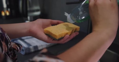 Woman Put Dishwashing Liquid On Sponge In The Kitchen. - close up