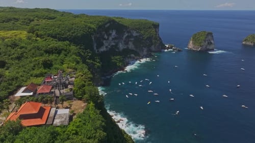 Aerial view of cliffside island with clear blue water and boats, Indonesia.