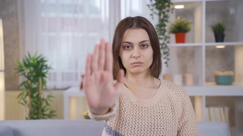 Zu Hause sagt die junge Frau Stopp mit ihrer Hand gegen Missbrauch und Vergewaltigung und schaut in die Kamera.