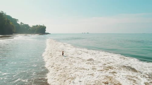 Woman wades through gentle surf along a sunny Costa Rica beach in the morning