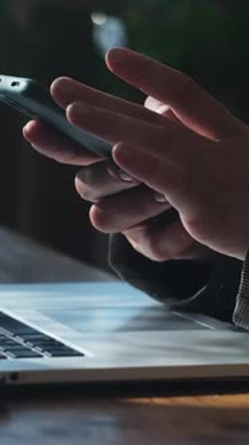 Hands Use Phone Above Laptop in Workplace