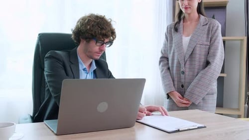 Young caucasian businessman using laptop while secretary giving document for signing at office.