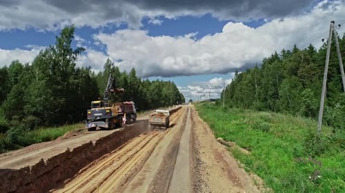Heavy machinery working in road construction in rural forest landscape, low altitude aerial view