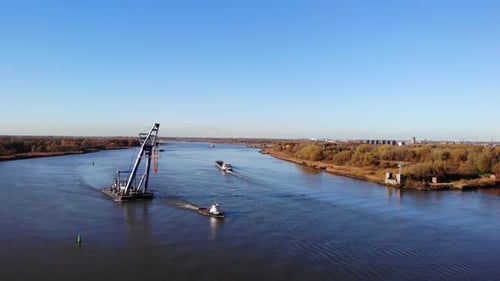 Tugboat Towing Bulk Carrier Loaded With Heavy Equipment Across The River In Barendrecht, Netherlands
