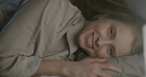 Portrait d'une belle jeune femme allongée dans son lit sur un oreiller moelleux souriant en regardant la caméra