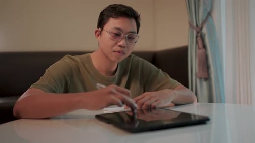 Focused on the task a young man with glasses concentrates intently on writing notes