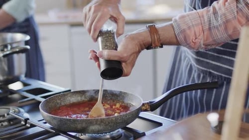 Man Adding Pepper to Sauce in Kitchen