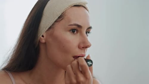 Young Woman Applying Lipstick in Front of Mirror