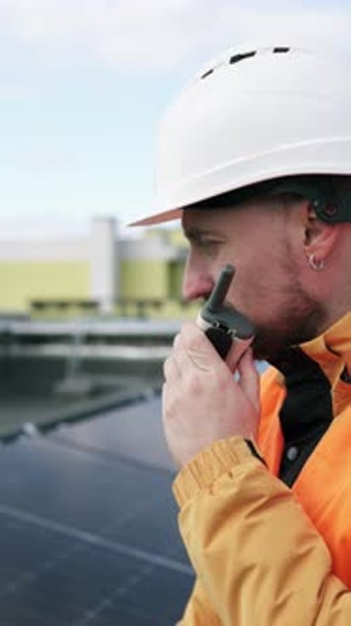 A solar panel installation engineer talks on a walkie-talkie on the roof of a building.