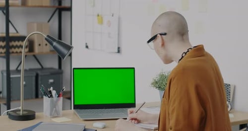 Businesswoman Writing Looking at Green Screen Chroma Key Laptop in Office