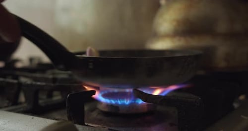 Primer plano de llama de fuego calentando sartén en cocina de casa friendo cebolla.