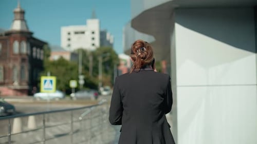 Back View of Woman in Suit Walking with Coffee on Phone Call in Urban Setting