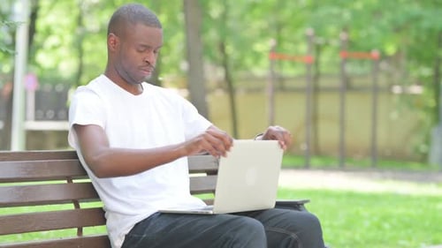Junger Afrikaner verlässt die Bank, nachdem er den Laptop im Freien geschlossen hat