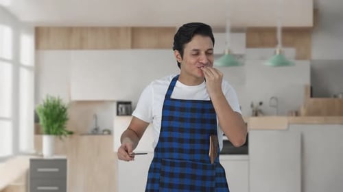 Man Tastes Food with Wooden Spoon in Kitchen