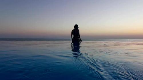 Beautiful Woman Relax in Infinity Swimming Pool at Luxury Hotel Spa Enjoy Golden Sunset View of