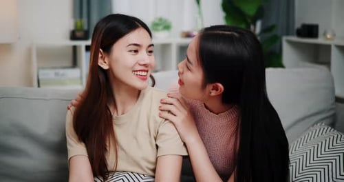 Two Smiling Women Embracing on a Couch Indoors