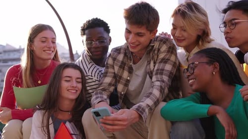 Low Angle View of Group of Caucasian Young People Looking Smiling Videos on Cell Phone Outdoors