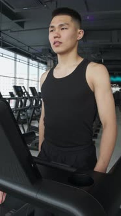 A Fit Young Guy is Walking on a Treadmill at the Gym During the Day Portrait