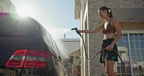 Woman Washing Black Car with Hose Outside Home