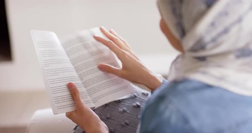 Mujer feliz en hijab leyendo un libro en el sofá de su casa con espacio para copiar, Cámara lenta