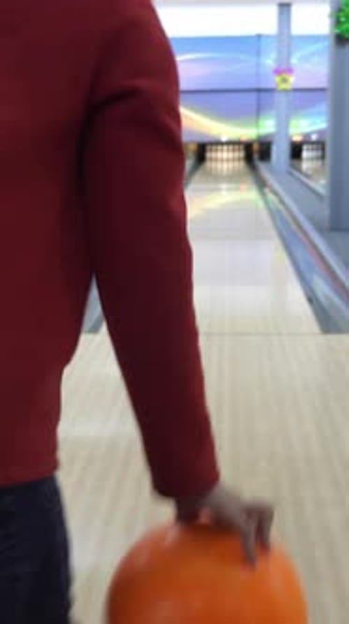 Orange Bowling Ball Rolling Down the Lane Towards the Pins in a Vibrant Bowling Alley with Colorful