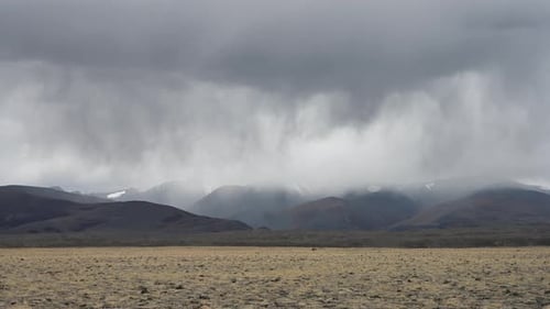 Thunderclouds and rain coming from snowy mountains over the steppe