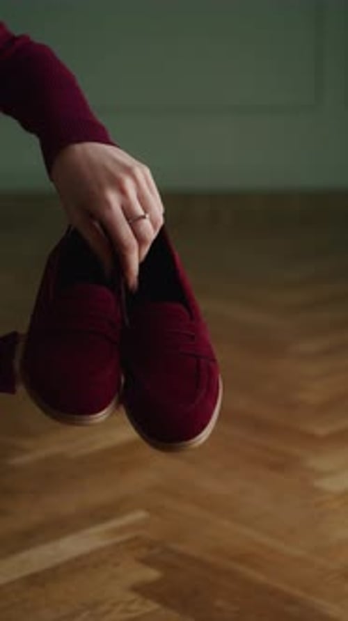 Hand Holding Burgundy Slipon Shoes Over Wooden Floor Product Presentation for Footwear Fashion with