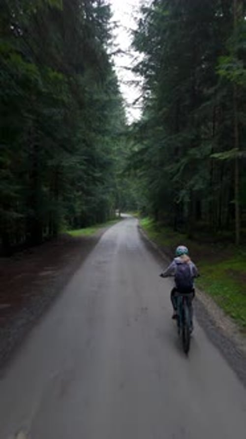Woman Riding E-Bike On Forest Path Surrounded by Green Nature, Tracking Vertical View