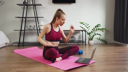 Training zu Hause: Junge Frau mit sportlicher Figur benutzt Laptop-Uhren, Video-Fitnessunterricht