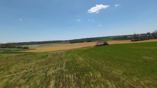 Green farm fields and Plowing at work during sunny day in American countryside. Fpv drone following
