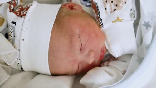 Beautiful newborn baby face in a cap. Caucasian child lies his head to camera. Close up.