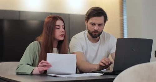 Couple Reviews Finances Using Laptop at Home