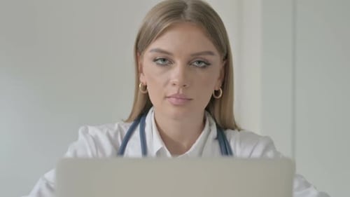 Close up of Female Doctor Looking at Camera while Working on Laptop in Clinic