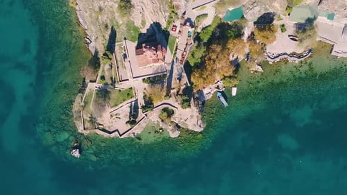 Monastery above a pristine turquoise lake spinning drone shot. Religious historic heritage building.