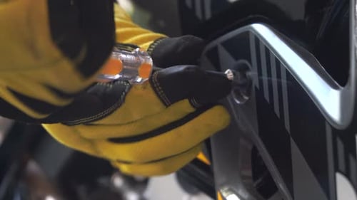 Mechanic's hands tightening a bolt head with a driver on the body of a motorcycle - close up focus p