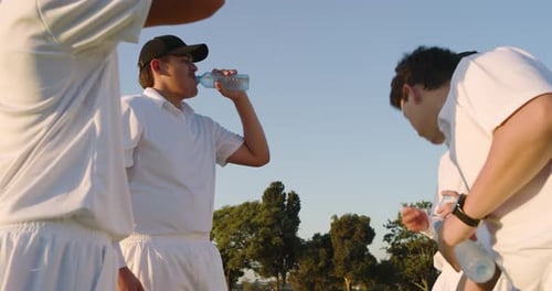 Rompe la intensa hidratación, diversos compañeros de equipo de críquet masculinos comparten botellas de agua en el campo de críquet