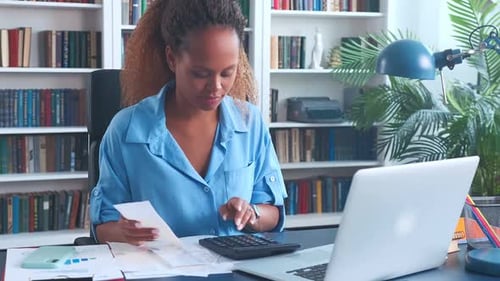 Young African American Woman Prepares Tax Reports Using Calculator and Laptop