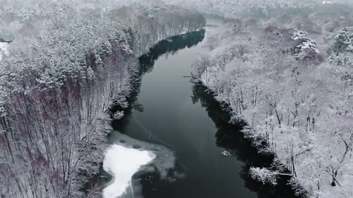 Aerial view of cold river and snowy forest in winter.
