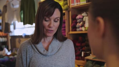 Yarn store owner explains knitting to customer in her small business