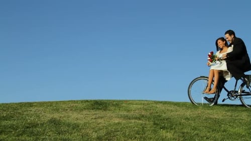 Happy Couple Riding Tandem Bicycle on Grassy Hill