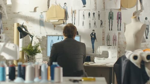 Vista posterior de un diseñador de moda masculino, trabajando en una computadora personal, tomando notas. Su lugar de trabajo