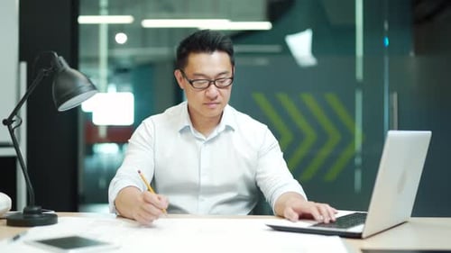 Asian creative designer or architect working in office at work using a laptop computer with drawings