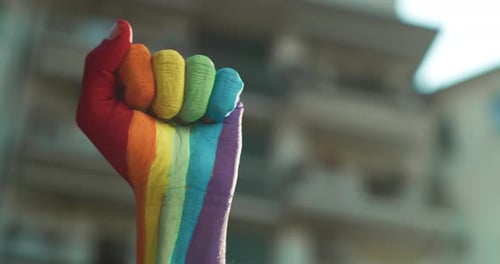 Plan cinématographique d'un homme de couleur arc-en-ciel de la LGBT Pride, la main levée avec le poing