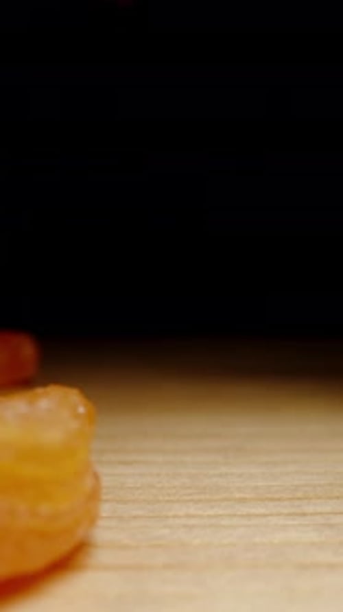 Vertical video. Dried Apricots Falls onto a Wooden Table Against a Black Background, in Slow Motion.