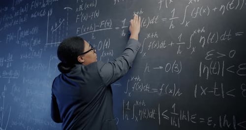 African American Maths Teacher Speaking Explaining Formula and Writing on Chalkboard in School