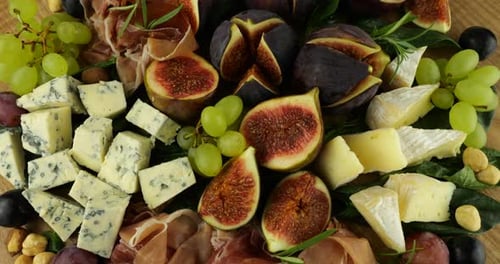 Figues, jamon, feuilles d'épinard, raisins, noix et fromages bleus sur une planche de bois. Set de snacks.