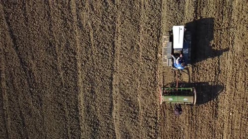 crawler tractor with seeder slowly advances on the land field, bird view aerial shot