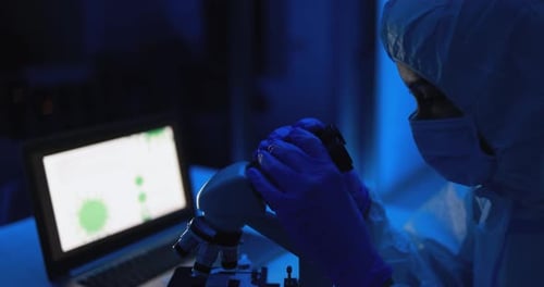 Female Scientist Using Microscope in Dark Lab