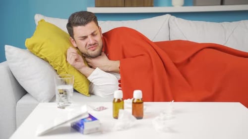 Homme malade allongé sur le canapé, malade, fatigué, épuisé et prenant péniblement ses médicaments.